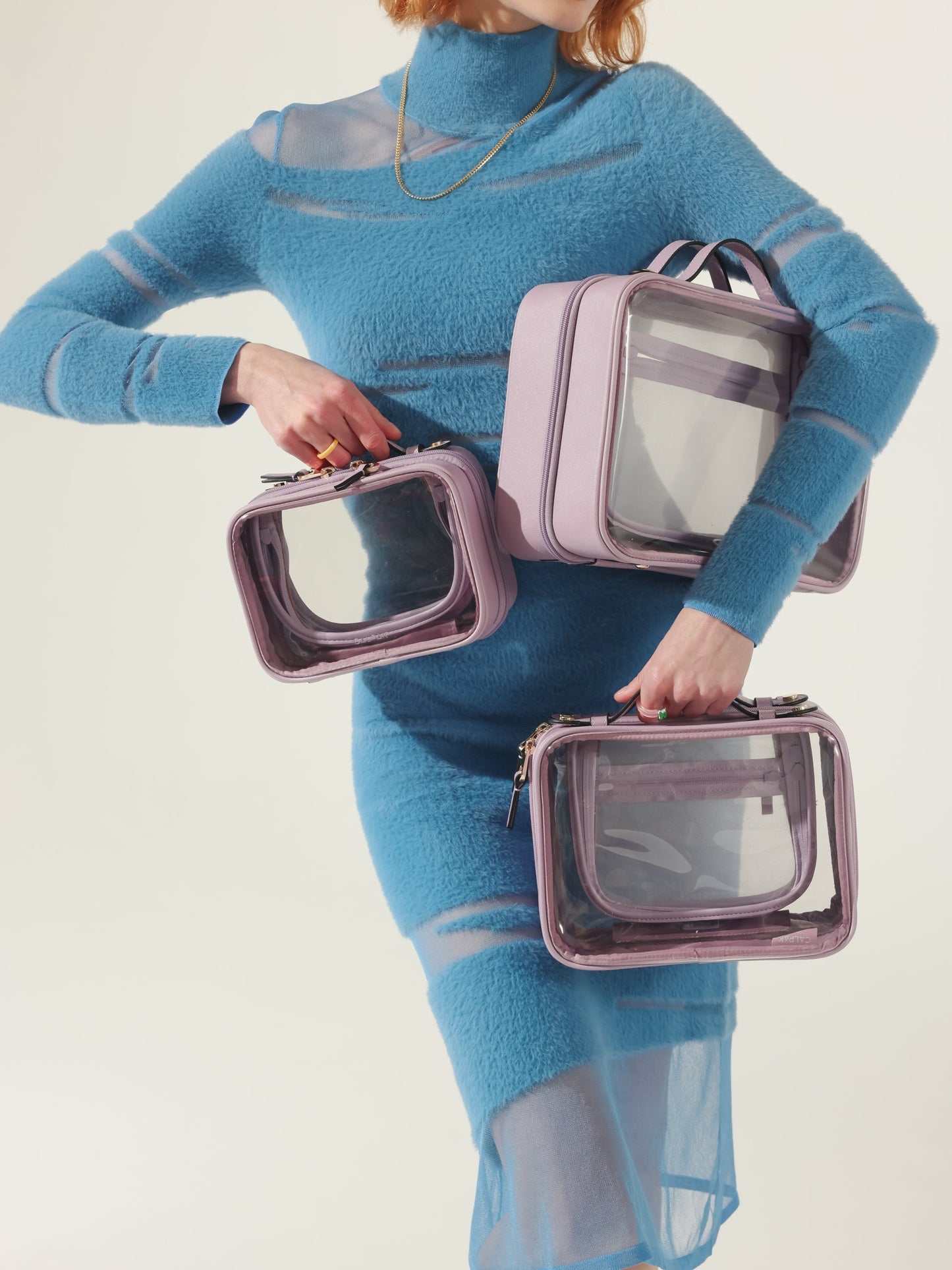 Model holding CALPAK clear makeup case in small, medium and large sizes in lavender purple; CMM2201-LAVENDER