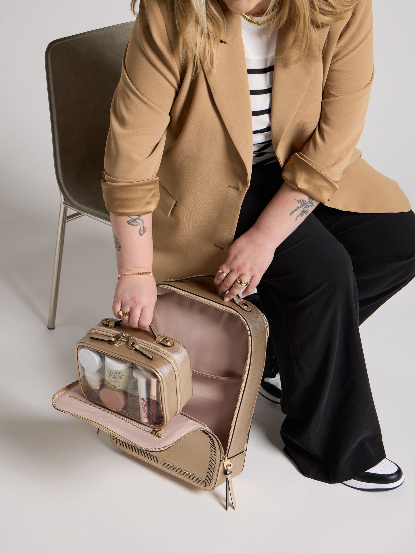 Model placing metallic gold small clear cosmetic case inside metallic gold CALPAK Kaya 15 inch Laptop Backpack; CCM2001-GOLD