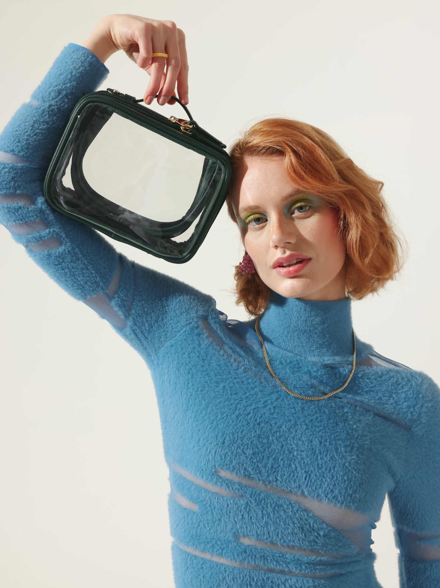 Model holding CALPAK small transparent makeup case with top handles in emerald; CCM2001-EMERALD